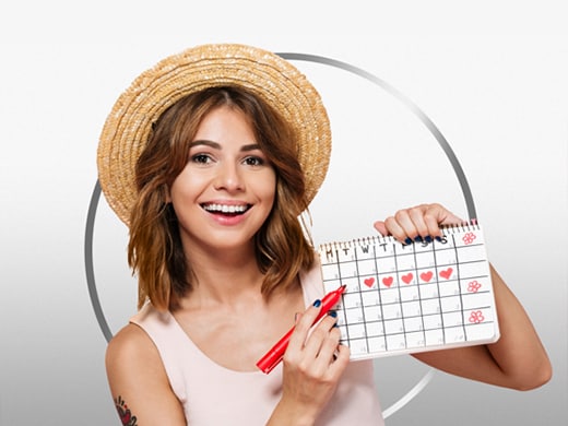 Une jeune femme brune souriante qui porte un T-shirt clair brandit un calendrier.